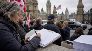 A woman signs a thick stack of petition pages on a stone ledge outside the Parliament buildings in Ottawa, Canadian flags and a crowd behind her