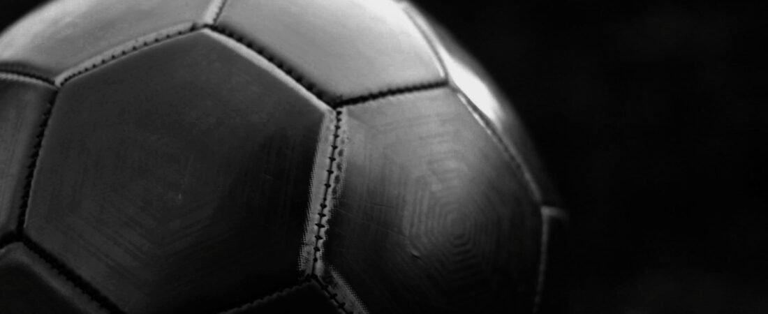 Close-up of a dark leather football showing the stitched seams between its curved panels