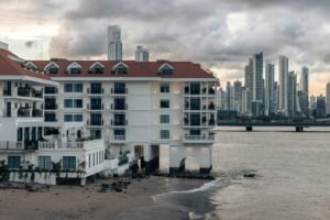 A white colonial building with a red tiled roof at the water's edge in Casco Viejo, Panama City, with the high rise towers of the modern financial district across the bay behind it