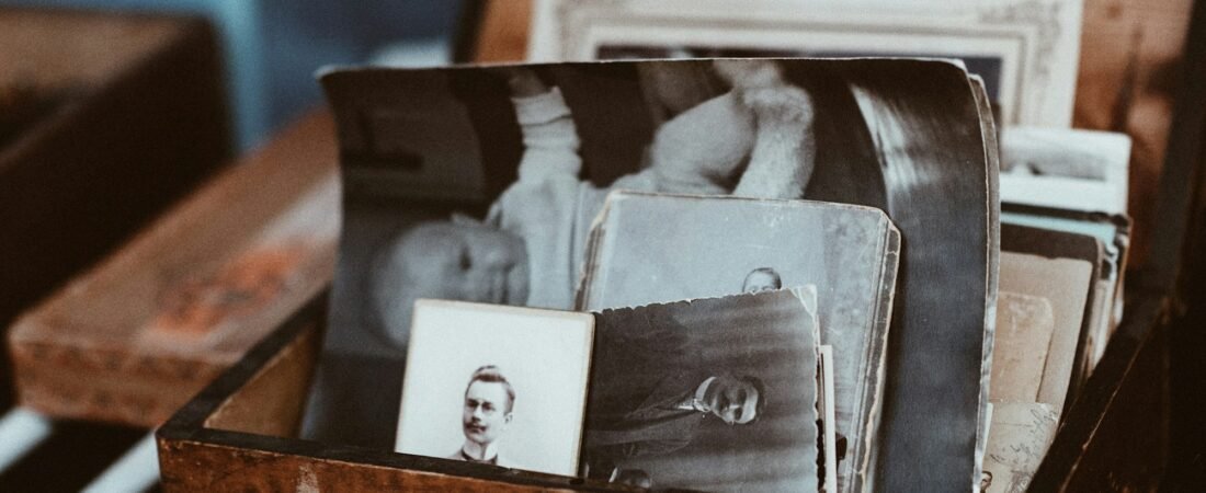 A wooden box on a table filled with old black and white photographs and card-mounted portraits, one of them leaning against the front edge of the box