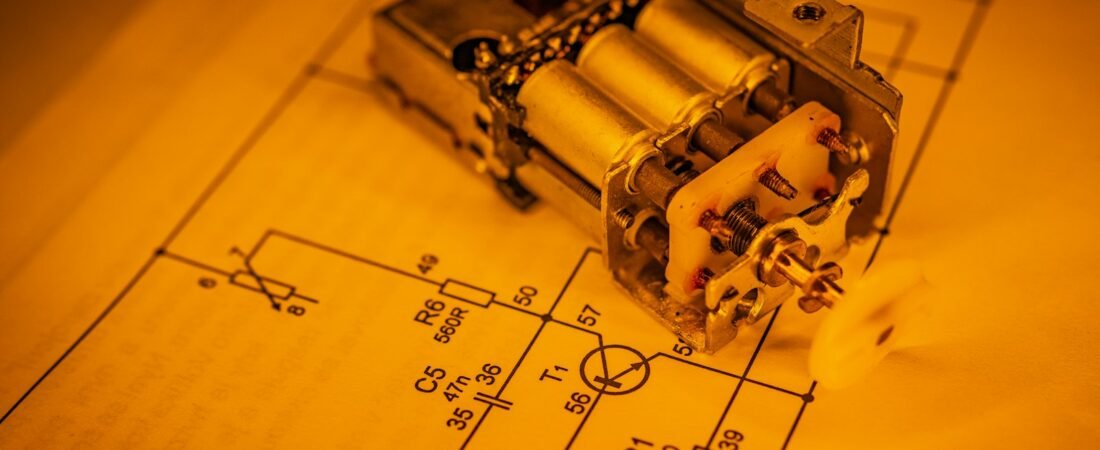 A small metal relay component sits on a printed circuit diagram, with resistor and capacitor labels such as R6 560R and C5 47n visible on the paper around it.