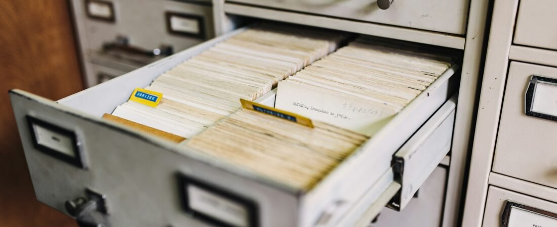 An open metal filing cabinet drawer packed with upright index cards and paper tabs, surrounded by other closed drawers