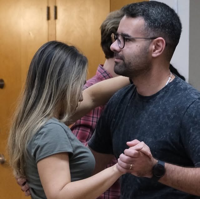 A couple dancing forro in close embrace at a Friday night class, with another couple in the background