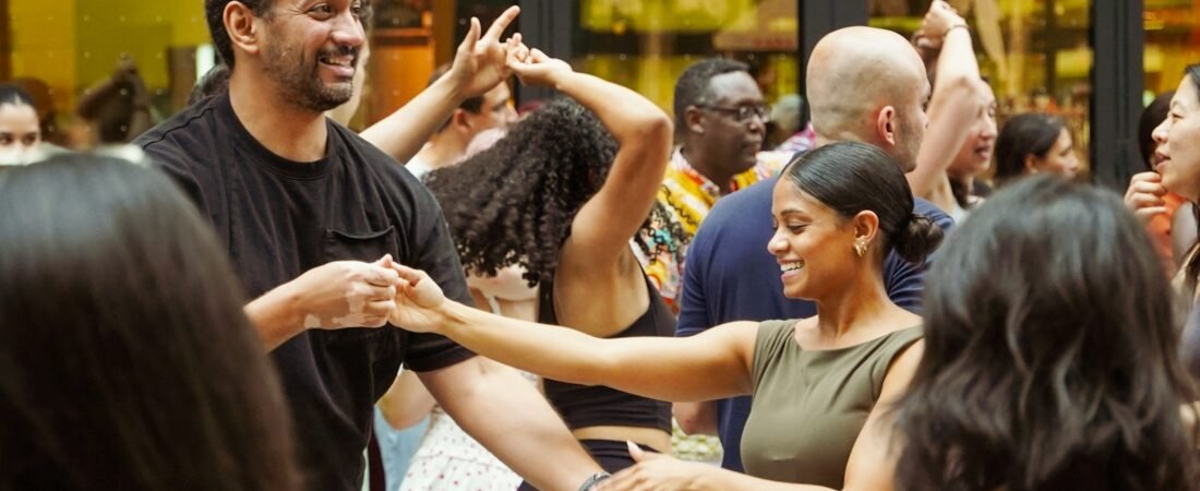A group of people dancing in pairs, holding hands, in a bright indoor venue