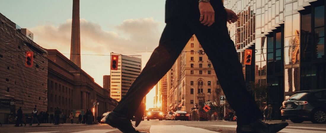 A person in a dark suit crosses a downtown Toronto street at sunset, with the CN Tower and Union Station in the background